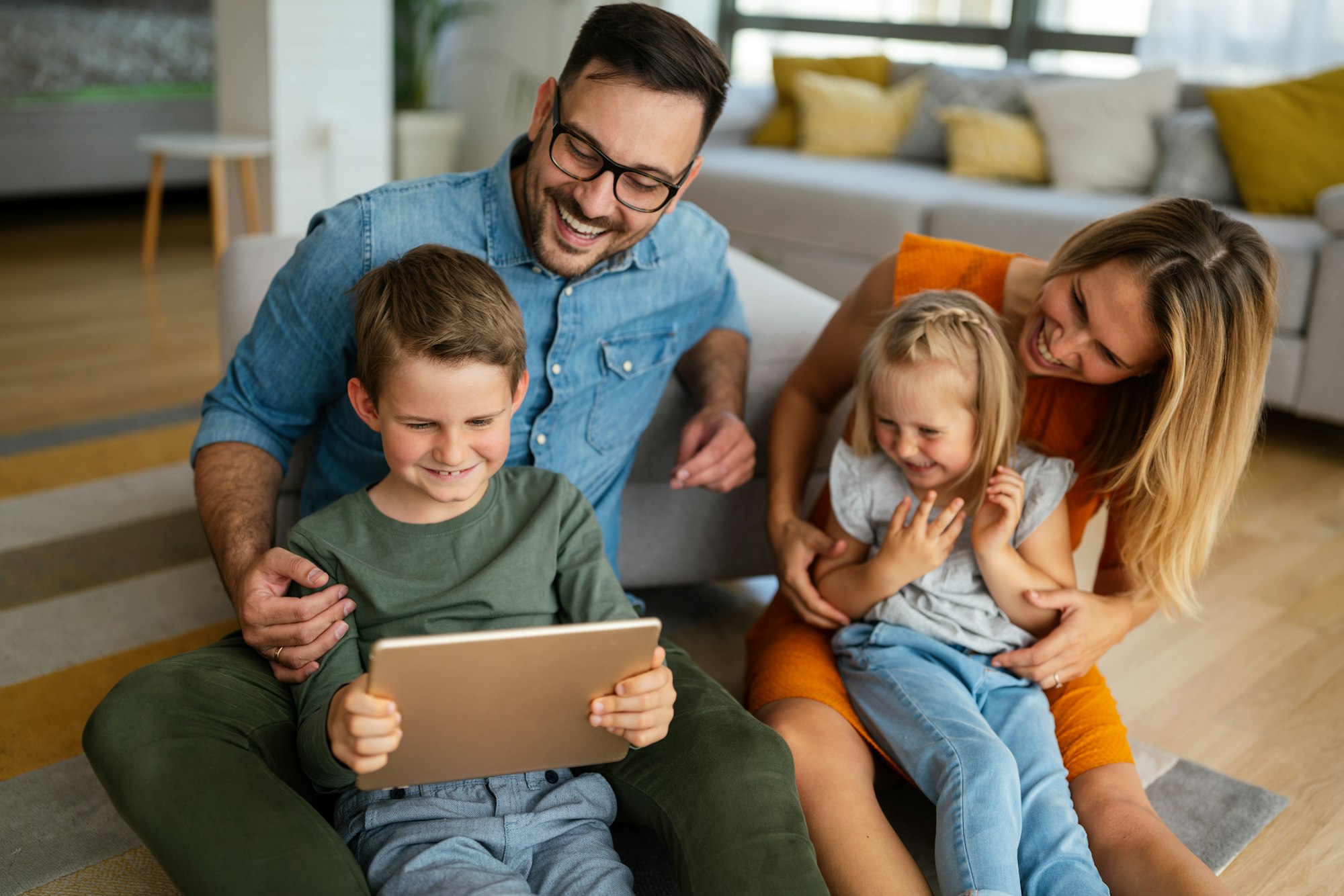 Happy young family having fun time at home. Parents with children using tablet